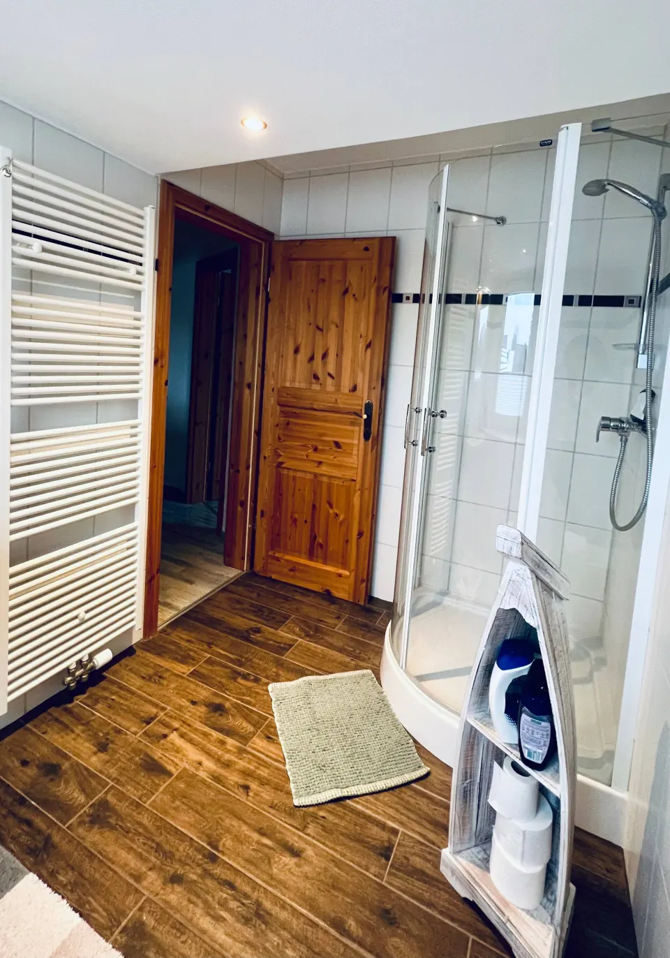 Badezimmer mit Glasdusche, Handtuchheizkörper und Holzoptikboden