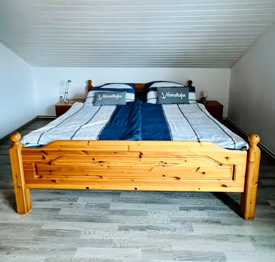 Doppelbett aus Kiefernholz mit blau-weißer Bettwäsche unter der Dachschräge