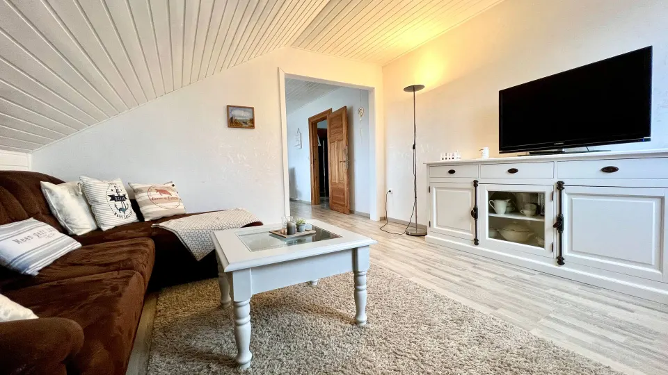 Wohnzimmer mit brauner Ledercouch, Fernseher und weißer Holzdecke